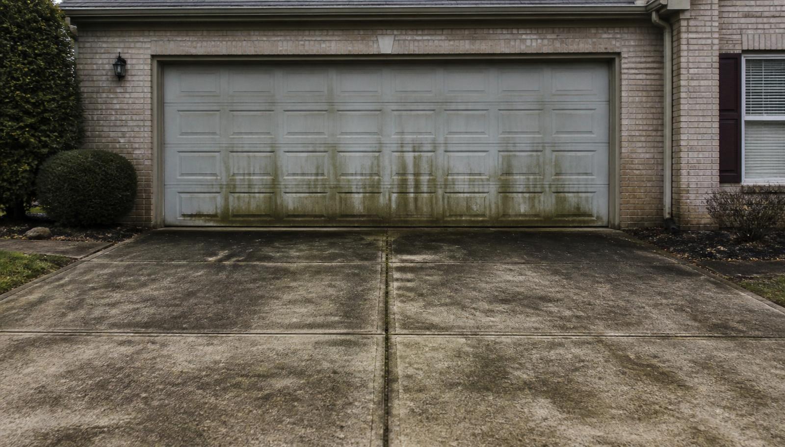 Grimy algae-stained concrete driveway and garage frontage before cleaning